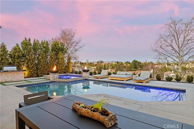 pool at dusk featuring an in ground hot tub, an outdoor kitchen, and a patio