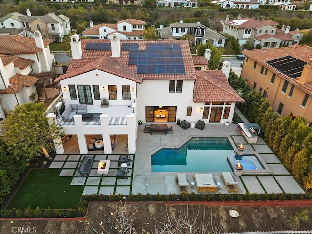 rear view of house featuring a patio, a tile roof, a chimney, an in ground hot tub, and roof mounted solar panels