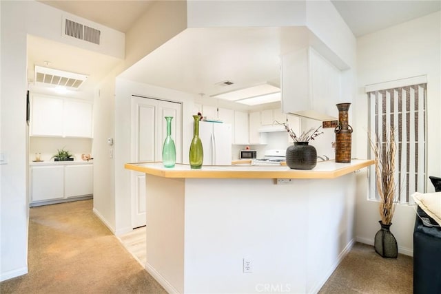 kitchen with white cabinetry, white refrigerator, kitchen peninsula, and stove