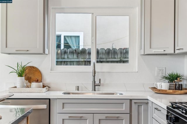 kitchen with light stone countertops, sink, dishwasher, and gray cabinets