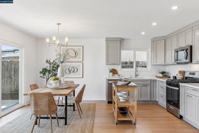 kitchen featuring light hardwood / wood-style flooring, hanging light fixtures, sink, gray cabinets, and stainless steel appliances