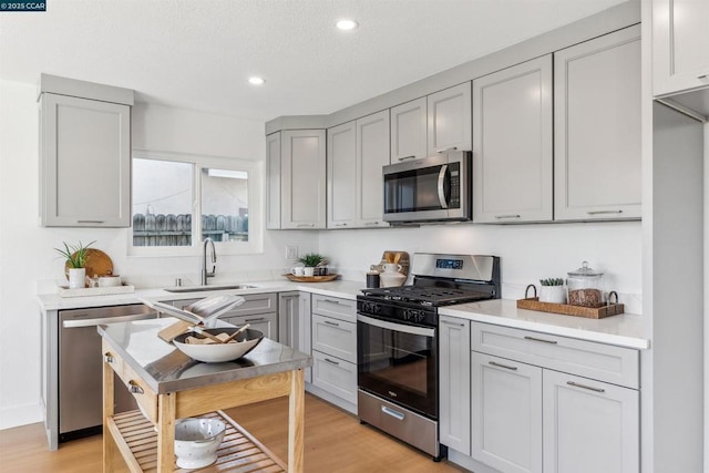 kitchen featuring sink, appliances with stainless steel finishes, gray cabinets, and light wood-type flooring