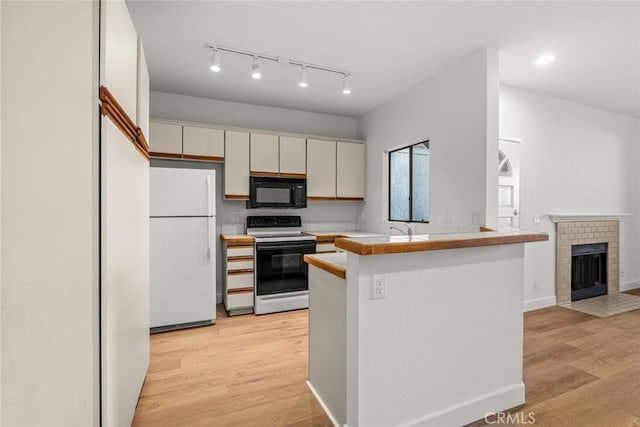 kitchen with white appliances, white cabinets, kitchen peninsula, light wood-type flooring, and a tiled fireplace