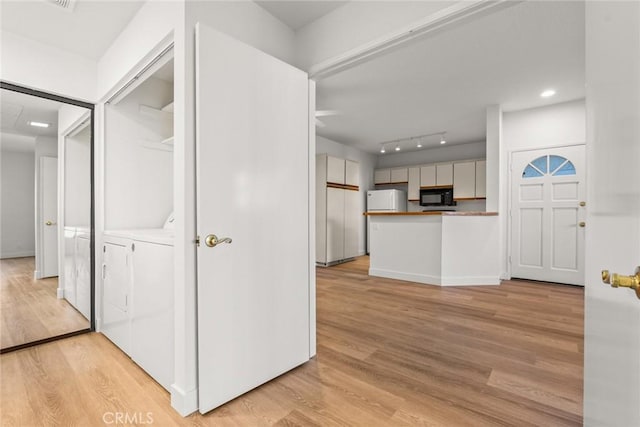 kitchen with independent washer and dryer, white cabinets, refrigerator, and light wood-type flooring