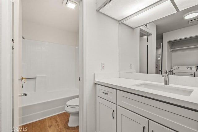 full bathroom featuring hardwood / wood-style floors, vanity, washing machine and clothes dryer, toilet, and bathtub / shower combination