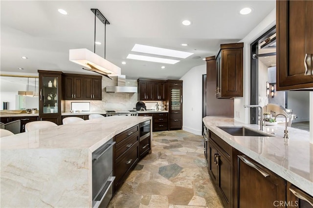 kitchen featuring decorative light fixtures, light stone countertops, stainless steel microwave, and sink