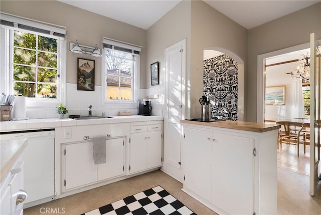 kitchen with white dishwasher, sink, white cabinetry, and a notable chandelier