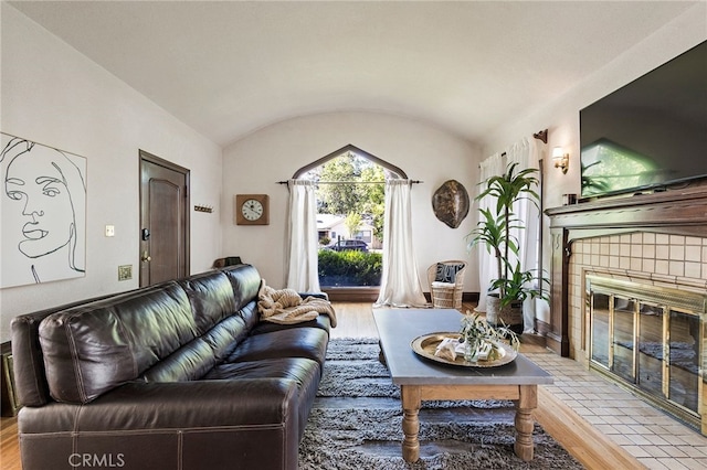 living room with a tile fireplace, vaulted ceiling, and light hardwood / wood-style floors