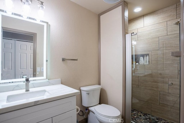 bathroom with a shower with shower door, toilet, and vanity