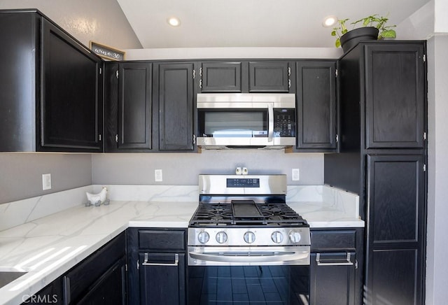 kitchen with light stone countertops, appliances with stainless steel finishes, and lofted ceiling