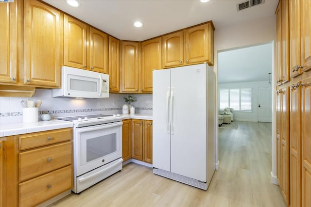 kitchen with decorative backsplash, white appliances, tile counters, and light wood-type flooring