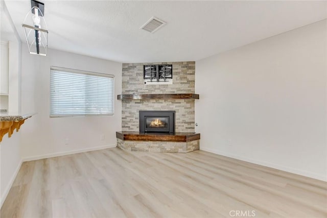 unfurnished living room with light wood-type flooring and a stone fireplace