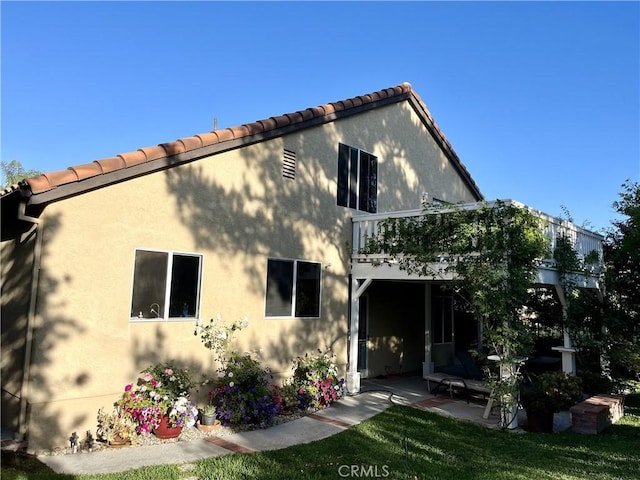 back of property featuring a balcony, a lawn, and a patio