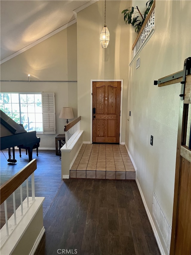 entryway with a barn door, dark hardwood / wood-style floors, high vaulted ceiling, and ornamental molding