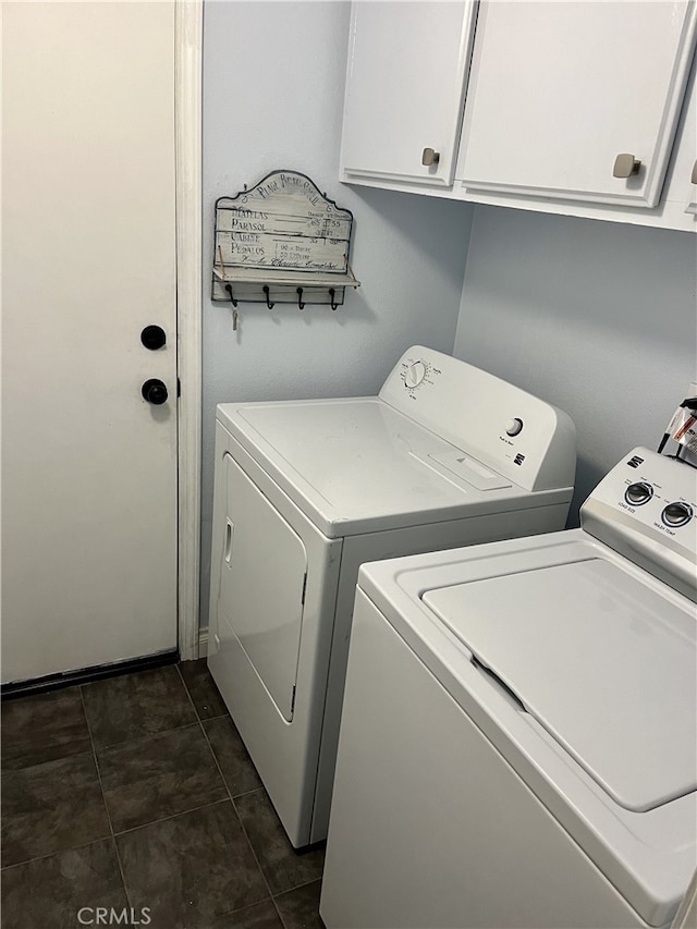 clothes washing area with cabinets, washer and dryer, and dark tile patterned floors