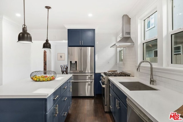 kitchen with high quality appliances, wall chimney exhaust hood, decorative light fixtures, sink, and blue cabinetry