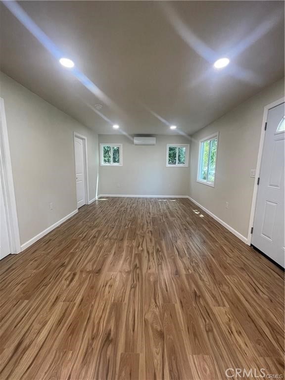 basement featuring a wealth of natural light, hardwood / wood-style floors, and a wall mounted AC