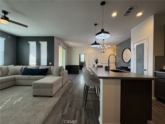 kitchen featuring sink, decorative light fixtures, a breakfast bar, dark hardwood / wood-style floors, and a center island with sink