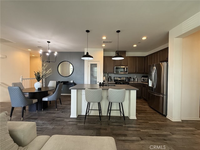 kitchen featuring appliances with stainless steel finishes, decorative light fixtures, tasteful backsplash, a center island with sink, and dark brown cabinets