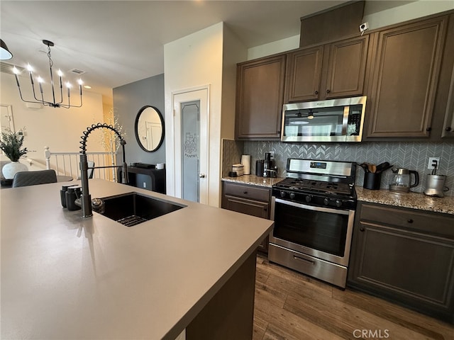 kitchen with appliances with stainless steel finishes, sink, decorative light fixtures, backsplash, and a center island with sink