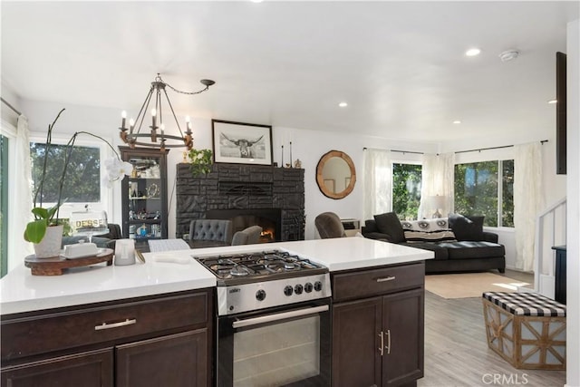 kitchen featuring stainless steel gas stove, light hardwood / wood-style flooring, hanging light fixtures, a stone fireplace, and dark brown cabinetry