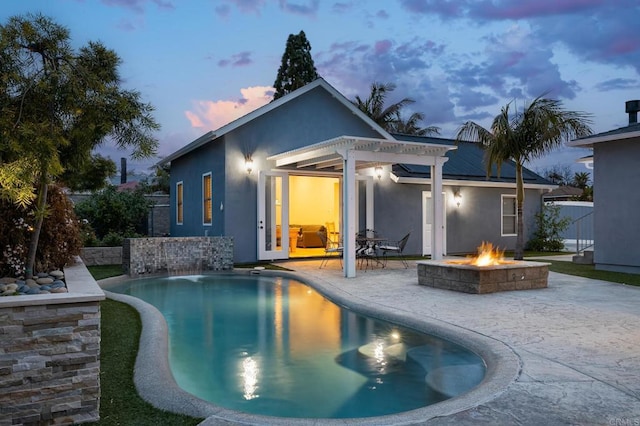 pool at dusk featuring an outdoor fire pit, a patio area, and a pergola