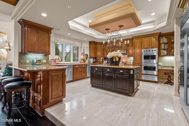 kitchen with pendant lighting, appliances with stainless steel finishes, a center island with sink, and a raised ceiling