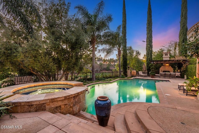 pool at dusk featuring an in ground hot tub, a patio area, and exterior fireplace