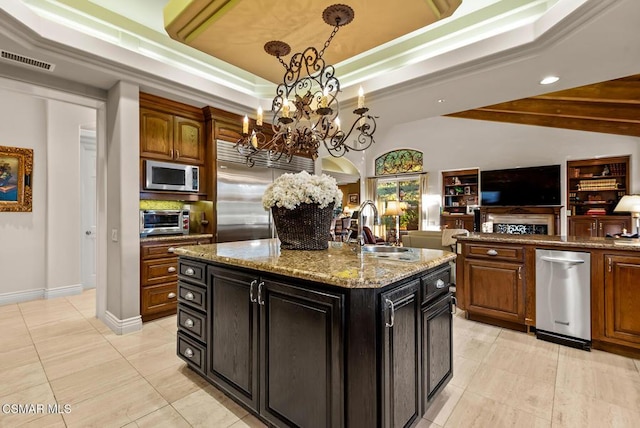 kitchen featuring a notable chandelier, light stone countertops, appliances with stainless steel finishes, sink, and an island with sink