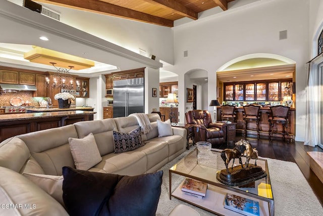 living room with a notable chandelier, wood ceiling, a high ceiling, beam ceiling, and dark wood-type flooring