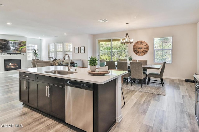 kitchen with pendant lighting, sink, a kitchen island with sink, light hardwood / wood-style floors, and stainless steel dishwasher