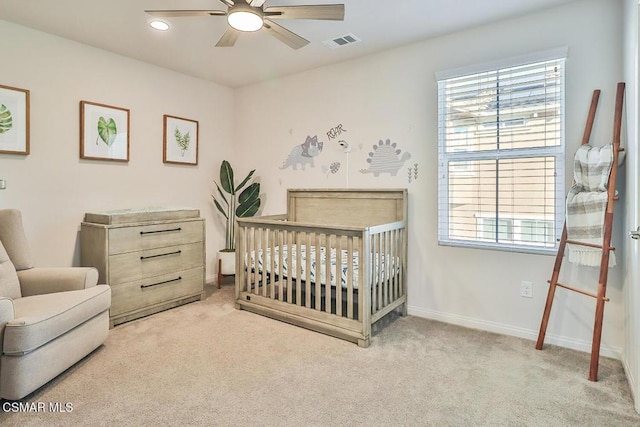 bedroom with a crib, light colored carpet, and ceiling fan