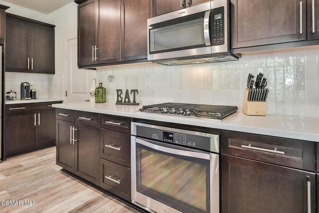 kitchen with backsplash, dark brown cabinetry, appliances with stainless steel finishes, and light wood-type flooring