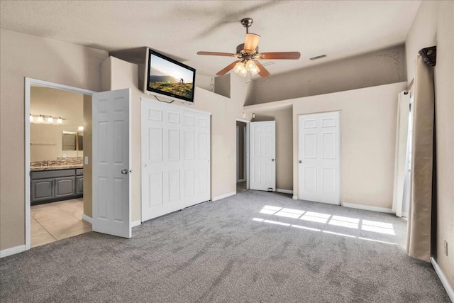 unfurnished bedroom with a closet, ceiling fan, light colored carpet, and ensuite bath