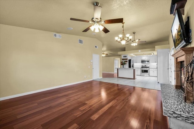 unfurnished living room with ceiling fan with notable chandelier, a fireplace, lofted ceiling, and light wood-type flooring