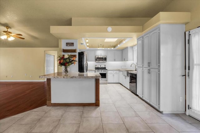 kitchen with sink, light tile patterned floors, light stone countertops, a center island, and stainless steel appliances