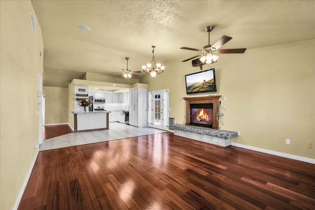 unfurnished living room with a textured ceiling, a fireplace, light wood-type flooring, ceiling fan with notable chandelier, and lofted ceiling