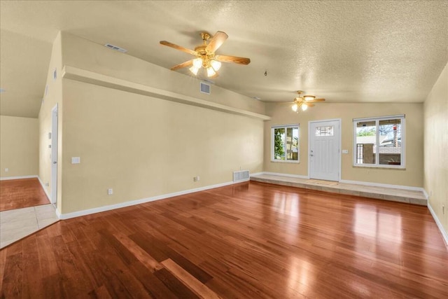 unfurnished living room with hardwood / wood-style floors, a textured ceiling, vaulted ceiling, and ceiling fan