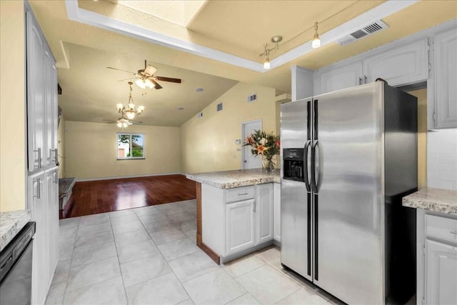 kitchen with white cabinets, a tray ceiling, stainless steel fridge, kitchen peninsula, and light tile patterned floors