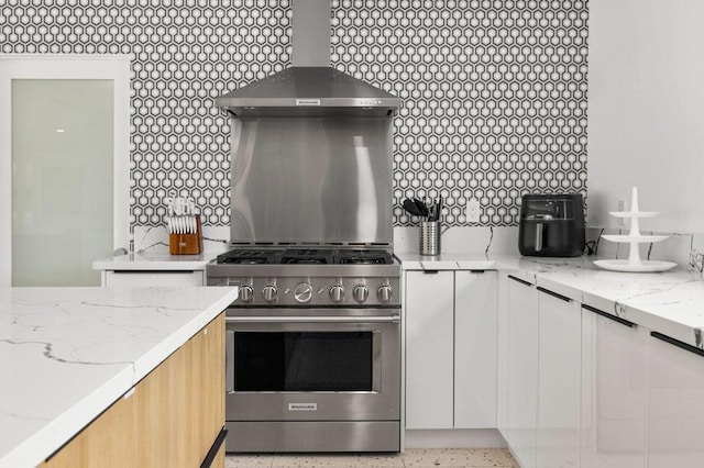 kitchen featuring high end stainless steel range oven, backsplash, white cabinetry, and wall chimney range hood