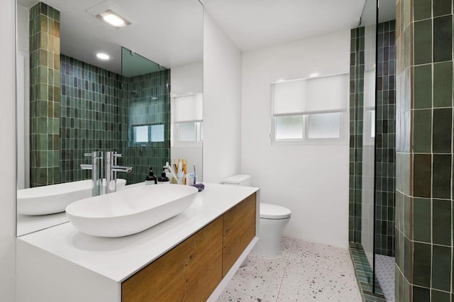 bathroom with a tile shower, toilet, and vanity