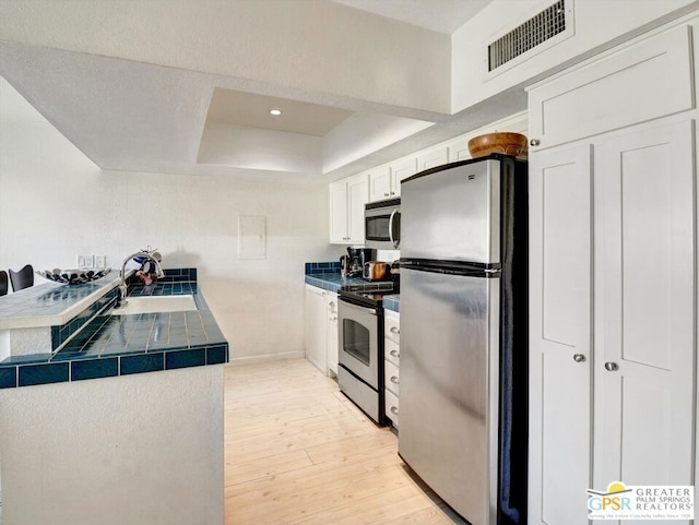 kitchen with a raised ceiling, sink, white cabinets, tile countertops, and stainless steel appliances