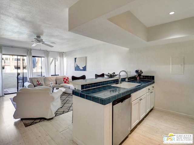 kitchen with tile counters, stainless steel dishwasher, white cabinets, sink, and kitchen peninsula