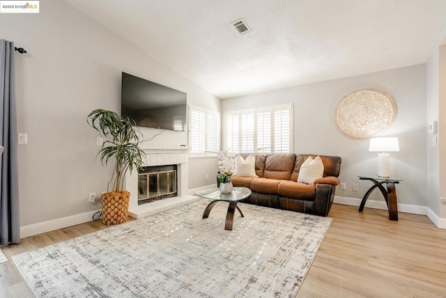 living room with light hardwood / wood-style floors, vaulted ceiling, and a brick fireplace