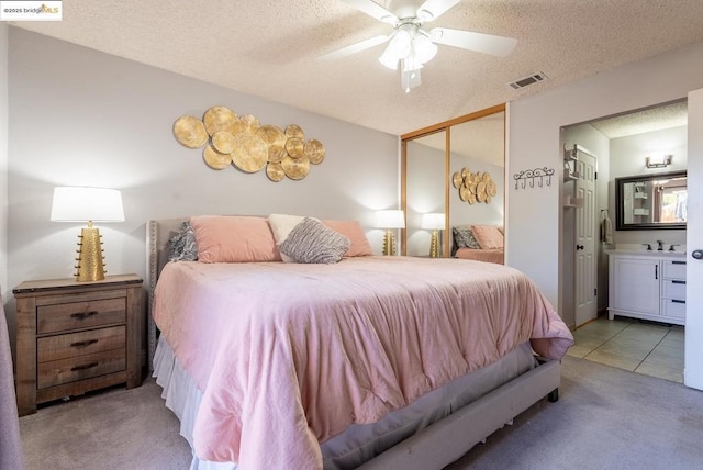 bedroom with light carpet, ceiling fan, a textured ceiling, connected bathroom, and a closet