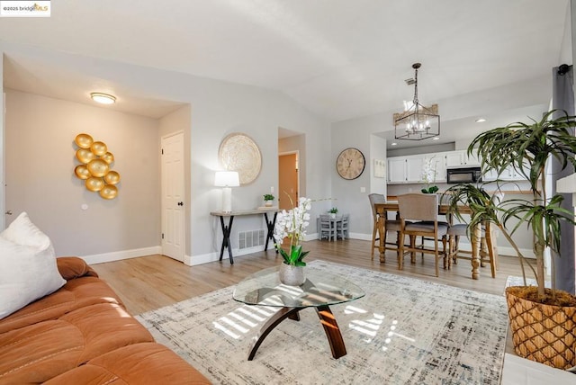 living room with vaulted ceiling, light hardwood / wood-style flooring, and an inviting chandelier