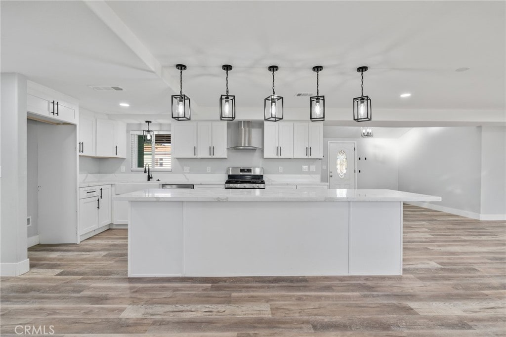 kitchen with pendant lighting, wall chimney range hood, stainless steel range with electric stovetop, white cabinetry, and a kitchen island