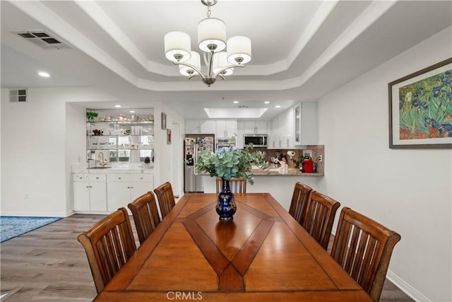 dining space featuring a raised ceiling, hardwood / wood-style flooring, and an inviting chandelier