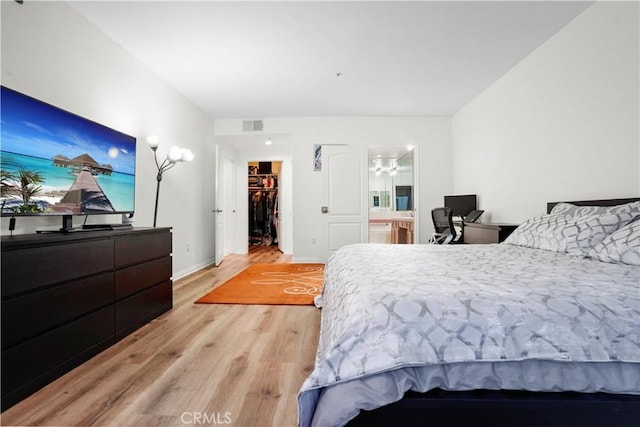 bedroom with ensuite bath, a spacious closet, a closet, and light hardwood / wood-style flooring