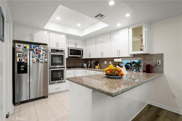 kitchen featuring white cabinetry, appliances with stainless steel finishes, kitchen peninsula, a raised ceiling, and backsplash